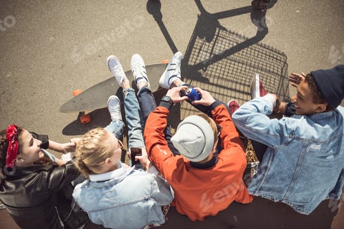 Preview: Overhead view of teenagers group sitting together and talking at skatepark