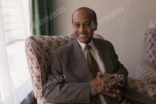 Preview: Front view of happy senior man with hand clasped looking at camera in home