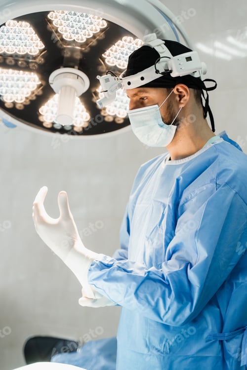 Preview: Male surgeon disinfects hands and wears surgical gloves preparing for surgery in medical clinic