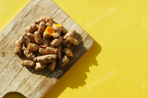 Preview: top view of turmeric root on a chopping board on yellow background