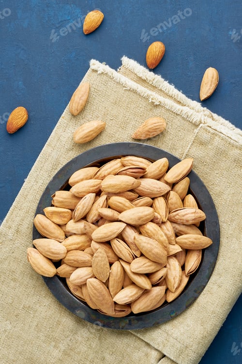 Preview: Top view plate with almonds in endocarp, bowl with drupe in shell on a linen napkin
