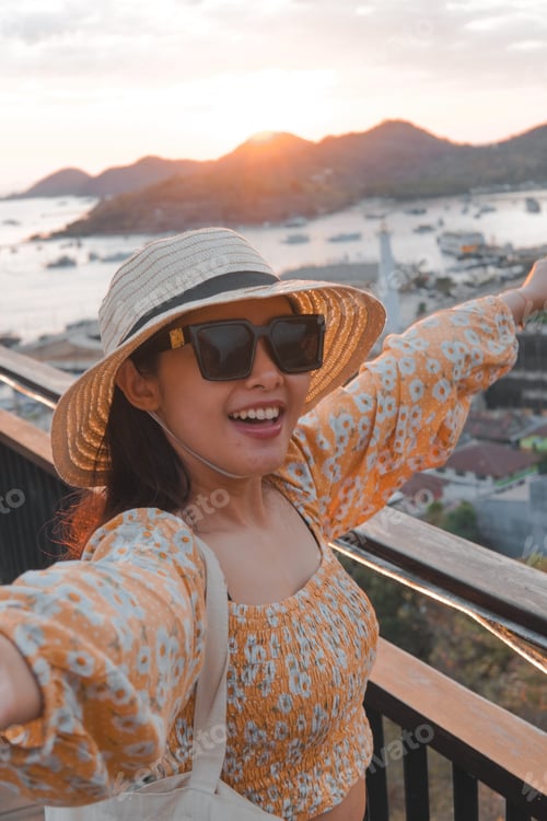 Preview: Joyful young Asian woman standing by the Labuan Bajo beach while pointing to the scenery.
