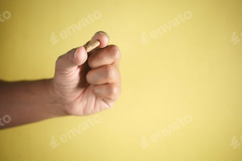 Preview: Hand holding a medical capsule against a yellow background