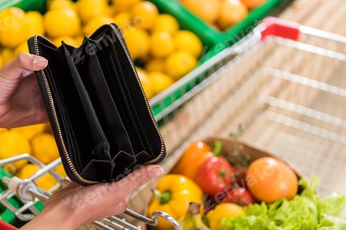 Preview: cropped image of woman showing empty wallet near shopping trolley in grocery store