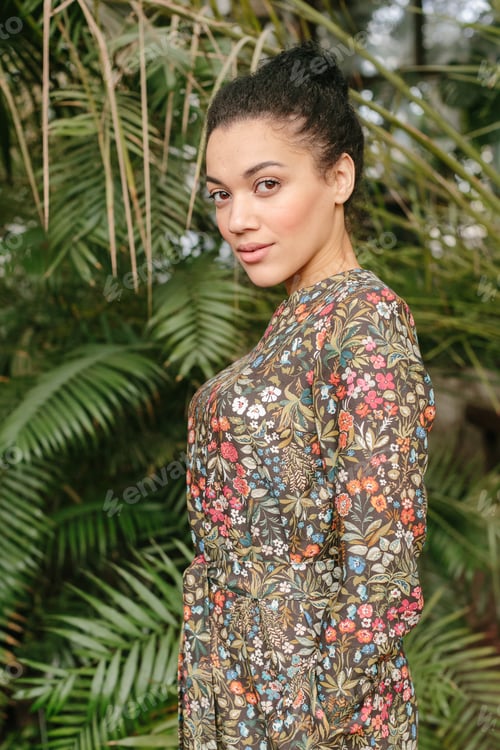 Preview: Portrait of smiling young black woman in dress with flowers pattern standing near glass