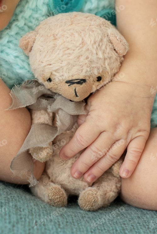Preview: vertical. newborn baby hand with hand-made teddy bear on a turquoise background
