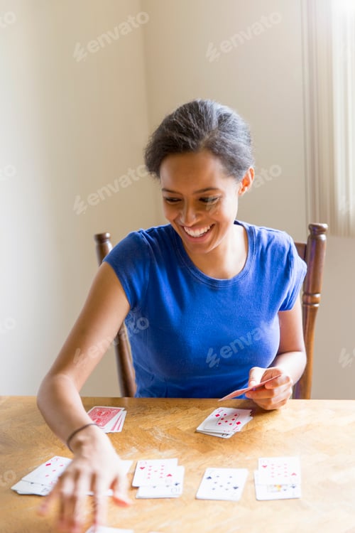 Preview: Young woman sitting at dining table playing cards smiling