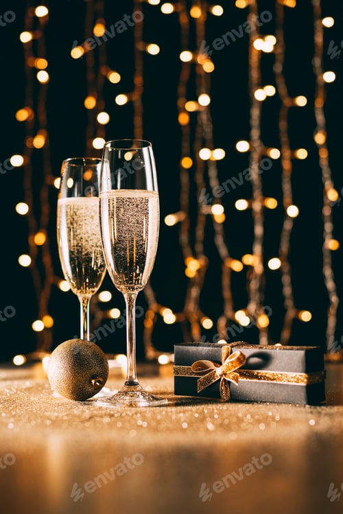 Preview: glasses of champagne, gift and bauble on garland light background, christmas concept