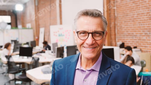 Preview: Portrait Of Mature Businessman In Modern Open Plan Office With Business Team Working In Background