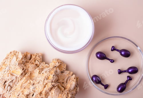 Preview: Top view of open box with white cream and cosmetics capsules in petri dish near it.