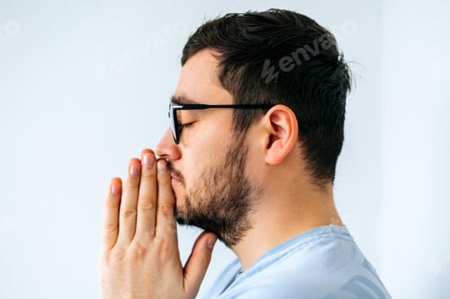 Preview: close up of a calm spiritual handsome american guy with glasess praying with closed eyes.