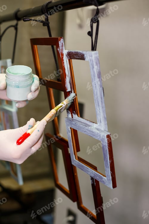 Preview: the master paints with a brush a wooden brown photo frame with light paint