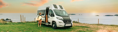 Preview: Woman with wetsuit and surfboard closing the door of her camper van to go surfing