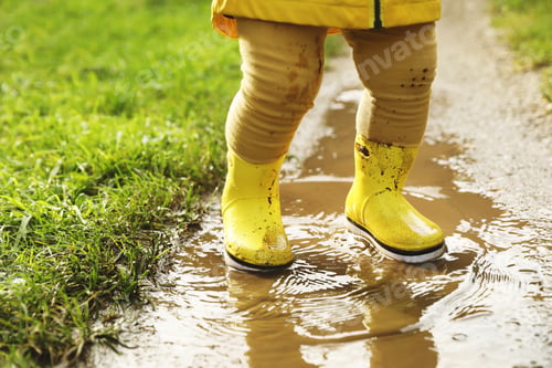 Preview: Little girl wearing rubber boots walking in puddle, closeup