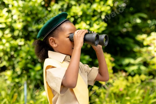 Preview: African american scout girl in uniform looking through binoculars in forest