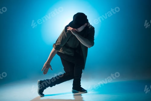 Preview: Young man dancer dancing funky hip hop on isolated studio neon blue background