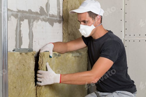 Preview: Worker in protective respirator mask insulating rock wool insulation in wooden frame