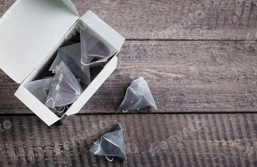 Preview: Tea bag shape of pyramid in paper packaging box on wooden table background. Top view with copy space