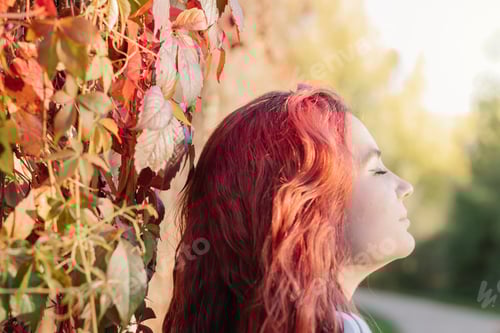 Preview: Relaxed young woman with red hair on an autumn day with her eyes closed breathing fresh air.