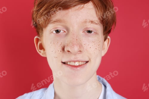 Preview: Smiling teenage boy with freckles on red background, closeup