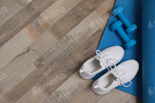Preview: Dumbbells, sneakers and mat on wooden floor, above view. Space for text