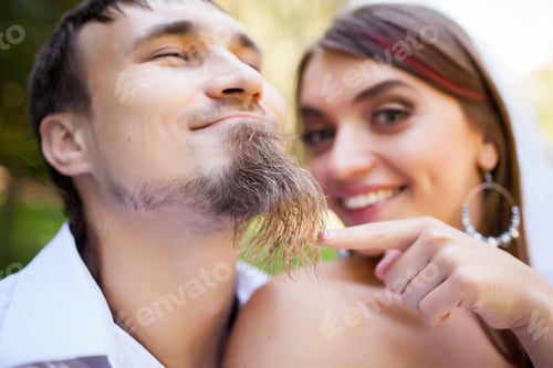 Preview: Cheerful bride brushing groom beard
