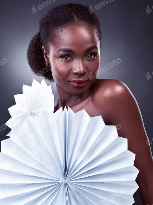 Preview: Studio portrait of a beautiful young woman posing with origami fans against a black background