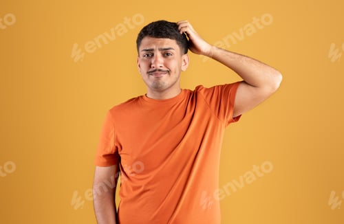 Preview: Sad pensive brazilian guy thinking and scratching head, posing isolated on orange background, studio