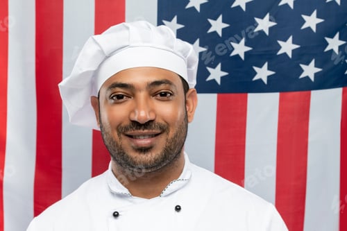 Preview: Young smiling chef of restaurant in white uniform standing in front of camera