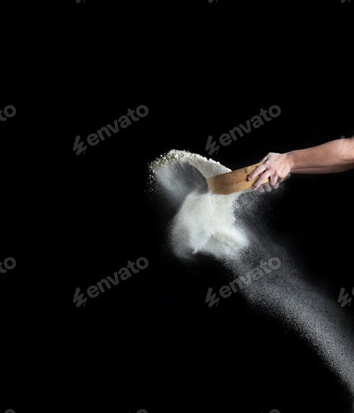 Preview: Female hand sifts white wheat flour through a round wooden sieve on a black background
