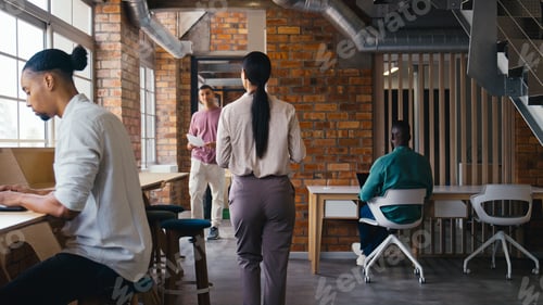 Preview: Busy Multi-Cultural Open Plan Office With Businesspeople Working At Desks And Meeting Colleagues