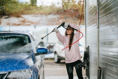 Preview: Young woman washing blue car at car wash