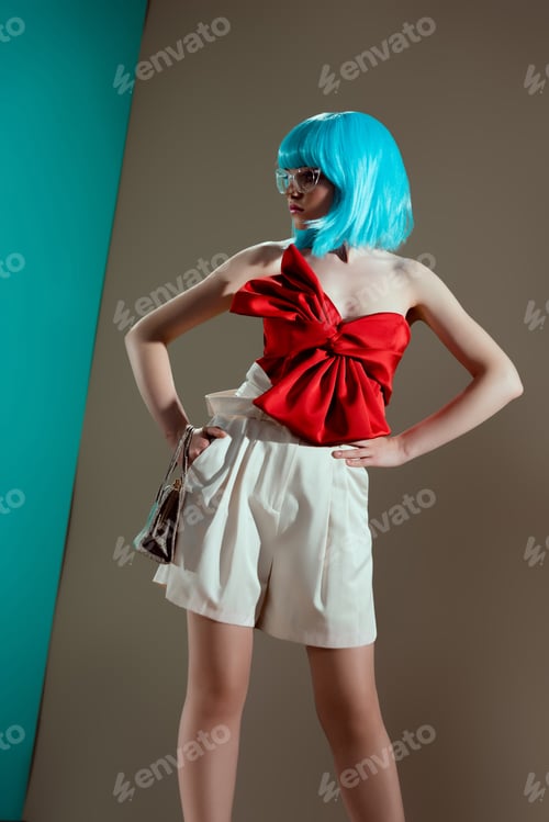Preview: beautiful fashionable girl in blue wig and red bow standing with hands on waist and looking away in