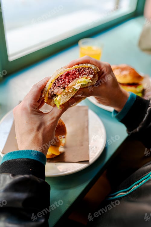 Preview: Customer enjoying delicious burger in restaurant with orange juice