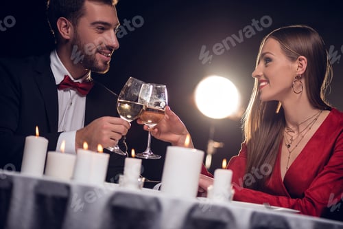 Preview: couple clinking with wine glasses on romantic date in restaurant