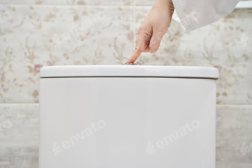 Preview: Asian male hand pressing toilet flush button in modern bathroom setting for hygiene and cleanliness