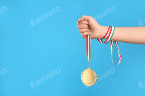 Preview: Woman holding gold medal on light blue background, closeup. Space for text