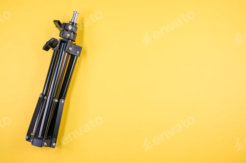 Preview: Closeup shot of a black iron folding tripod on a yellow background with a copy space