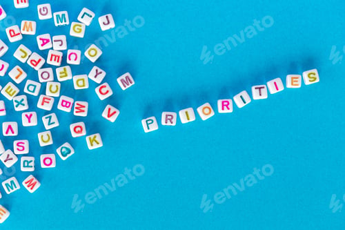 Preview: Word priorities made out of square beads on bright blue background next to pile of random letters