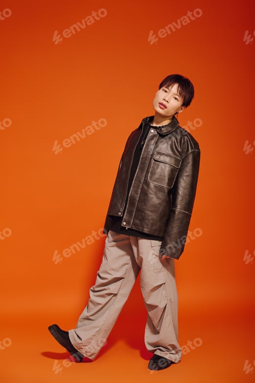 Preview: Stylish young Asian man poses confidently against a vibrant orange backdrop