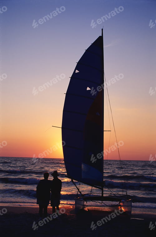 Preview: Silhouette of couple and dinghy on beach at sunset