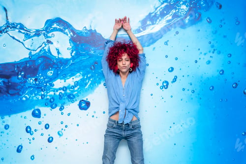 Preview: portrait of a young latin woman with red afro hair leaning on a blue background with blue drops