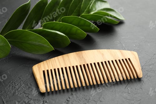 Preview: Wooden comb and branch with leaves on dark textured table, closeup