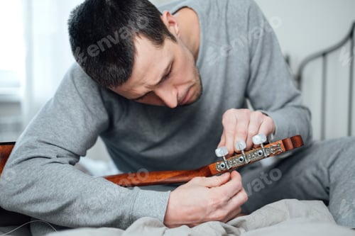 Preview: Young man changing a string on a guitar