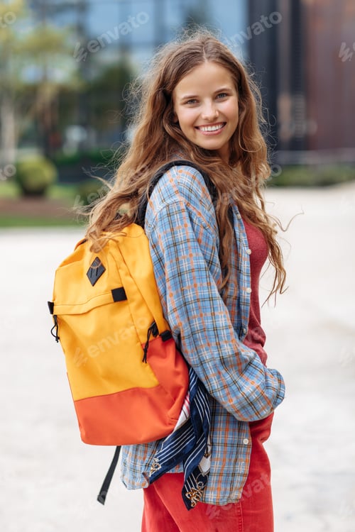 Preview: Stylish young blonde hipster woman student with backpack looking back to camera with happy face.