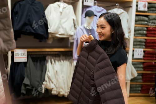 Preview: Asian woman shopping for winter jacket in clothing store