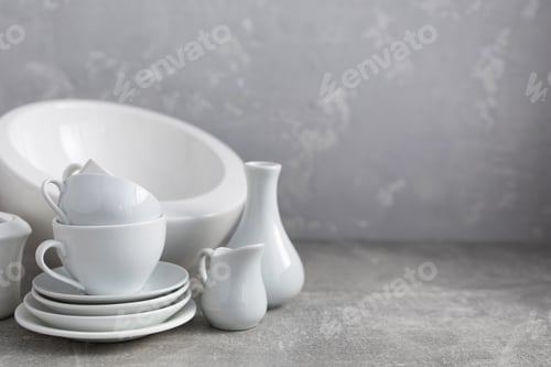 Preview: Empty crockery set or ceramic dishes. White kitchen dishware and tableware on table near grey wall