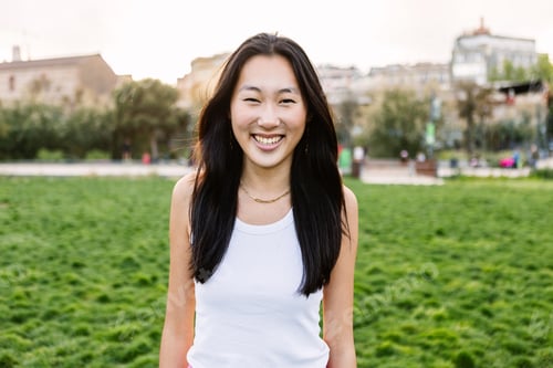 Preview: Outside portrait of young asian woman with toothy smile standing in city park.