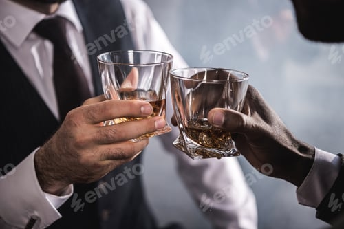 Preview: Close-up partial view of two men in formal wear clinking whiskey glasses