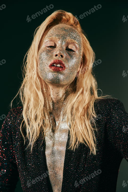 Preview: portrait of blonde woman with glitter on face and body posing in shiny dress on black backdrop